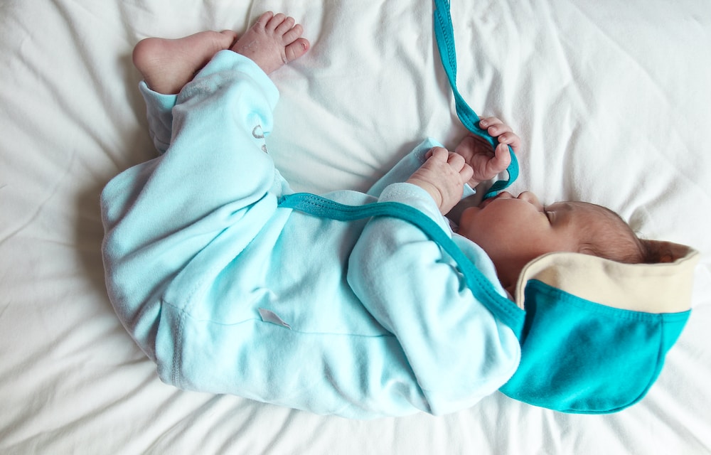 baby in teal onesie lying on bed