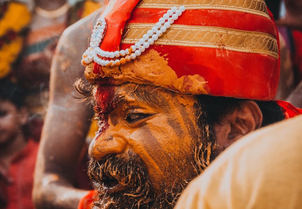 man in gold and red striped head dress with painted face